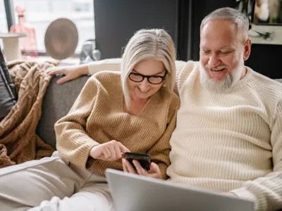 Ouder koppel kijkt op telefoon en laptop