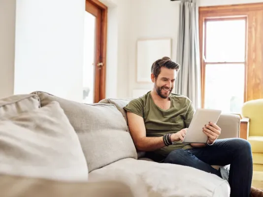 Un homme regarde sa tablette assis sur son canapé